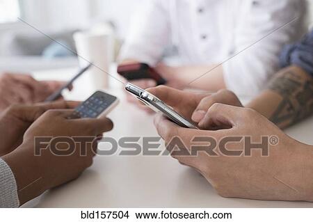 Picture - Close up of friends texting with cell phones at table. Fotosearch