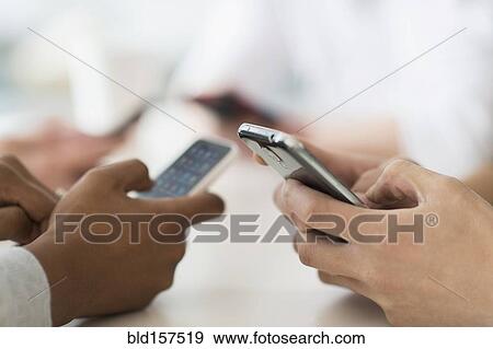 Stock Photo - Close up of friends texting with cell phones at table. Fotosearch