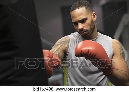 Stock Photo - Close up of Hispanic man punching bag in gym. Fotosearch
