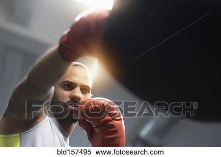 Stock Photography - Close up of Hispanic man punching bag in gym. Fotosearch