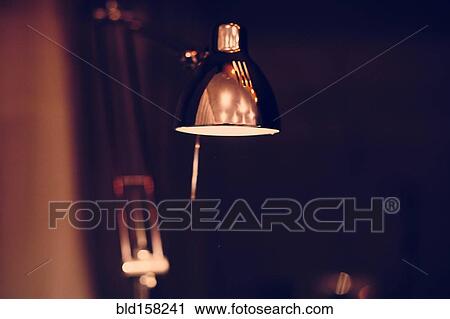 Stock Image - Close up of illuminated desk lamp at night. Fotosearch