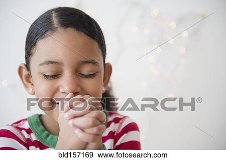 Stock Photo - Close up of mixed race girl praying at Christmas. Fotosearch