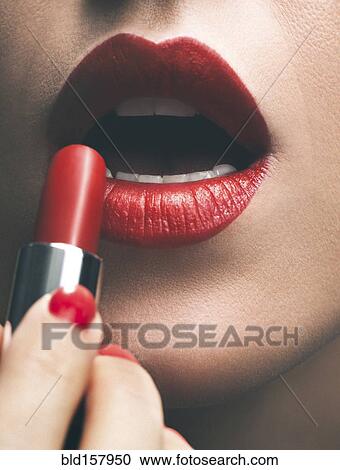 Stock Image - Close up of woman applying red lipstick. Fotosearch