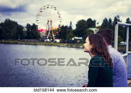 Couple standing at waterfront near ferris wheel View Large Photo Image Picture - Couple standing at waterfront near ferris wheel. Fotosearch