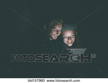 Couple wearing warm clothing using digital tablet at night View Large Photo Image Stock Image - Couple wearing warm clothing using digital tablet at night. Fotosearch