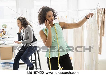 Stock Image - Dressmaker talking on cell phone in office. Fotosearch