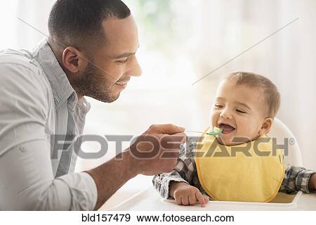 Stock Photo - Father feeding baby son in high chair. Fotosearch