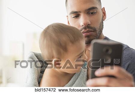 Stock Image - Father holding baby son and using cell phone. Fotosearch