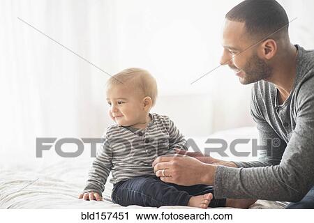 Stock Image - Father playing with baby son on bed. Fotosearch