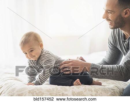 Stock Image - Father playing with baby son on bed. Fotosearch
