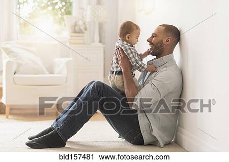 Stock Image - Father playing with baby son on floor. Fotosearch