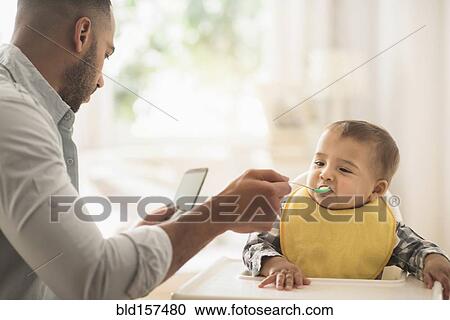 Father texting on cell phone and feeding baby son View Large Photo Image Stock Image - Father texting on cell phone and feeding baby son. Fotosearch
