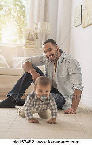 Stock Image - Father watching baby son crawling on floor. Fotosearch