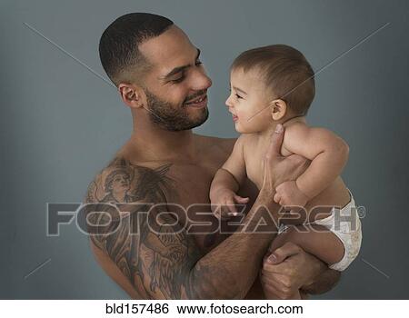 Stock Photograph - Father with tattoos holding baby son. Fotosearch
