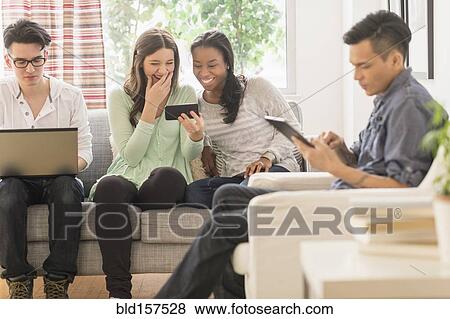 Stock Photo - Friends using technology in living room. Fotosearch