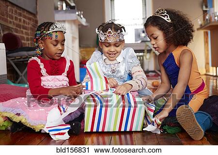 Stock Image - Girls with tiaras opening gifts at party. Fotosearch