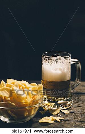 Stock Image - Glass of beer with bowl of potato chips. Fotosearch