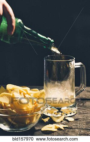 Hand pouring glass of beer near potato chips View Large Photo Image Stock Image - Hand pouring glass of beer near potato chips. Fotosearch
