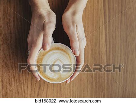 Stock Image - Hands holding cup of coffee with leaf drawn in milk. Fotosearch