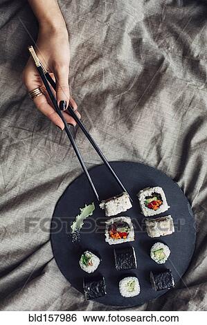 Stock Photograph - Hands of woman reaching for platter of sushi on bed. Fotosearch