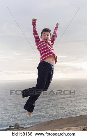 Stock Photograph - Hispanic boy jumping for joy on beach. Fotosearch