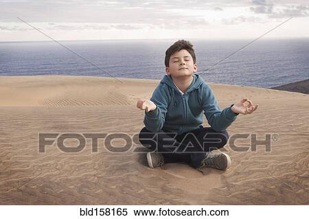 Stock Photography - Hispanic boy meditating on sand dune over ocean. Fotosearch