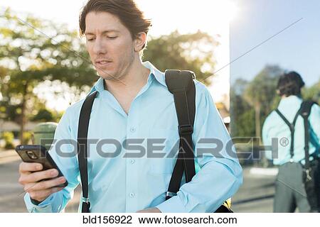 Stock Image - Hispanic businessman texting on cell phone outdoors. Fotosearch