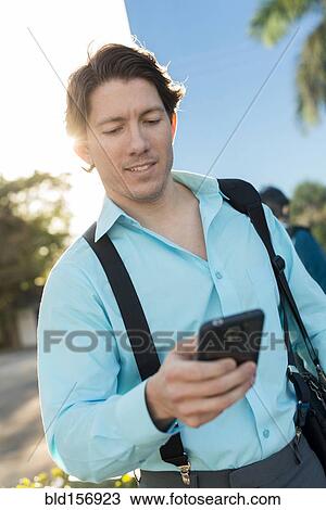 Stock Image - Hispanic businessman texting on cell phone outdoors. Fotosearch