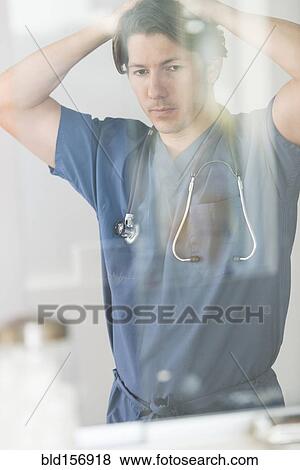 Stock Photo - Hispanic doctor with hands on head thinking in hospital. Fotosearch