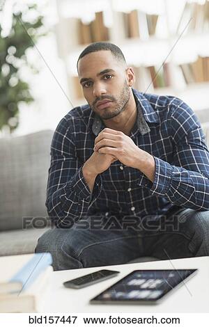 Stock Photo - Hispanic man with cell phone and digital tablet in living room. Fotosearch
