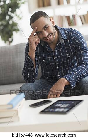 Stock Photo - Hispanic man with cell phone and digital tablet in living room. Fotosearch