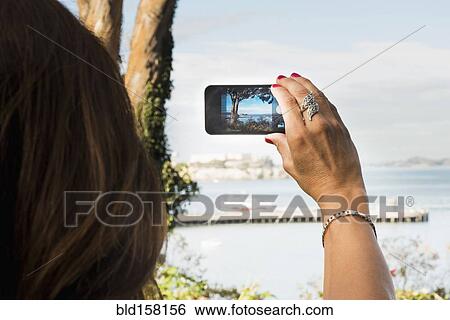 Stock Photograph - Hispanic woman taking cell phone photograph of beach. Fotosearch