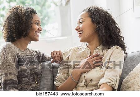 Stock Image - Laughing women talking on sofa. Fotosearch