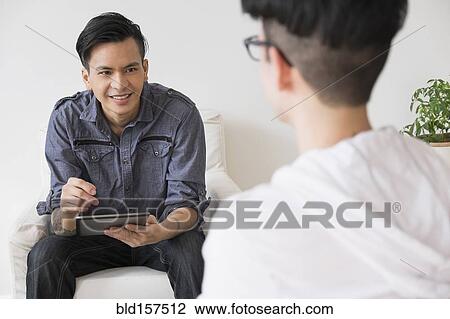 Stock Image - Men using digital tablet in living room. Fotosearch