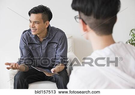 Stock Image - Men using digital tablet in living room. Fotosearch
