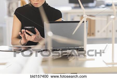 Stock Image - Mixed race architect with windmill models using cell phone. Fotosearch