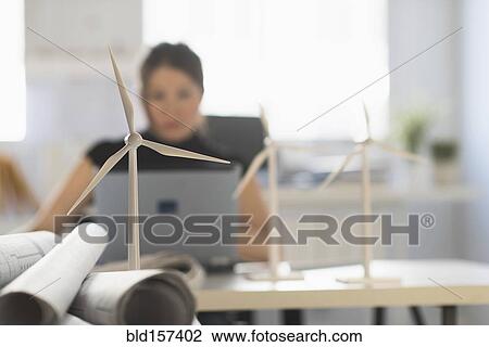 Stock Image - Mixed race architect with windmill models using laptop. Fotosearch