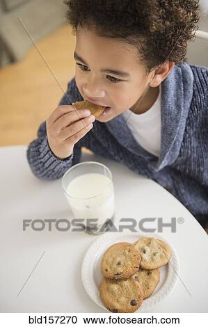 Stock Image - Mixed race boy eating cookies and milk. Fotosearch