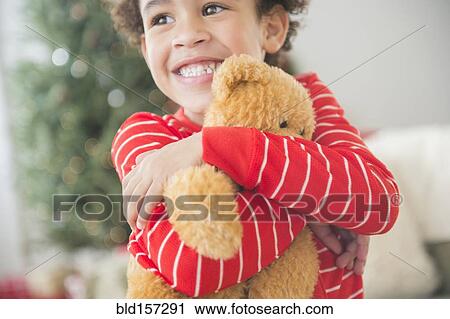 Stock Image - Mixed race boy hugging teddy bear at Christmas. Fotosearch