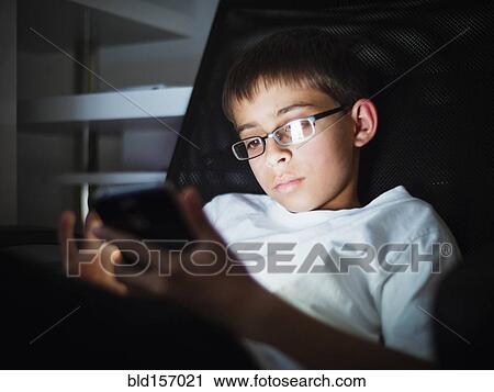 Stock Image - Mixed race boy texting on cell phone at night. Fotosearch