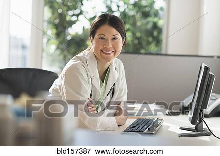 Stock Photo - Mixed race doctor smiling at computer in hospital. Fotosearch