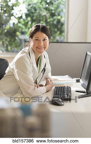 Mixed race doctor smiling at computer in hospital View Large Photo Image Stock Photograph - Mixed race doctor smiling at computer in hospital. Fotosearch