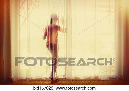 Stock Image - Mixed race girl behind curtain looking out window. Fotosearch