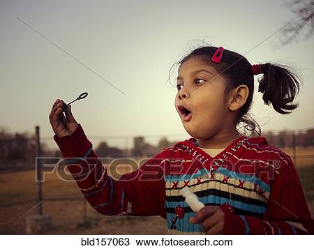 Stock Image - Mixed race girl blowing bubbles in field. Fotosearch