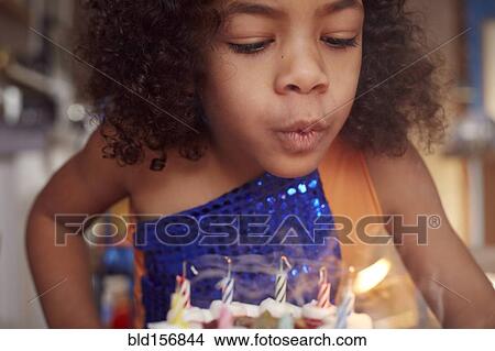 Picture - Mixed race girl blowing out cake candles. Fotosearch