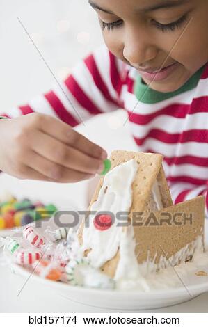 Picture - Mixed race girl decorating gingerbread house. Fotosearch