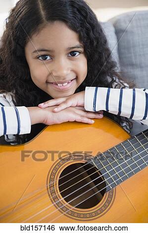 Stock Photograph - Mixed race girl holding guitar on sofa. Fotosearch