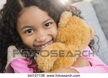 Stock Photo - Mixed race girl hugging teddy bear on sofa. Fotosearch