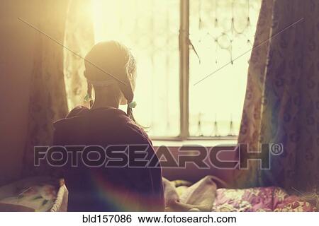 Stock Photograph - Mixed race girl looking out bedroom window. Fotosearch