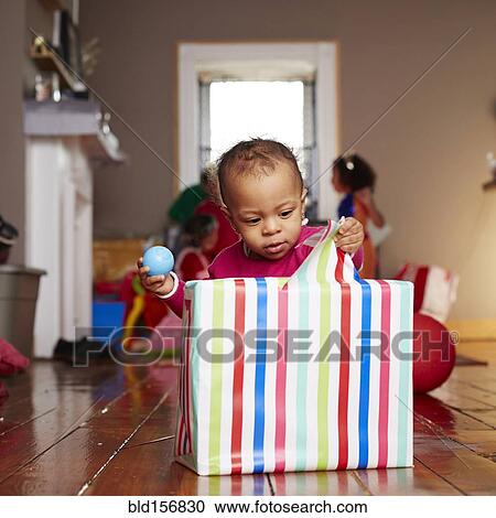 Stock Image - Mixed race girl opening gift in living room. Fotosearch